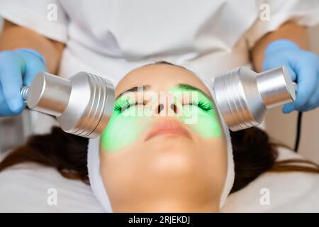 Fermer la main esthéticienne appliquant la luminothérapie à la jeune femme dans le salon de beauté. Banque D'Images