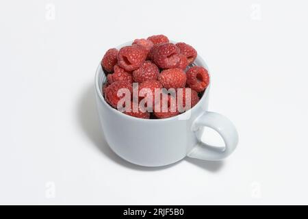 Grande tasse grise remplie à ras bord de framboises fraîches sur fond blanc Banque D'Images