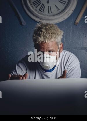 Maître masculin aux cheveux blonds sérieux concentré faisant et vérifiant la planche de surf blanche tout en observant et en touchant dans l'atelier Banque D'Images