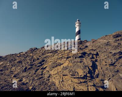 D'en bas d'un phare blanc situé au sommet de formations rocheuses rugueuses sous un ciel bleu sans nuages Banque D'Images