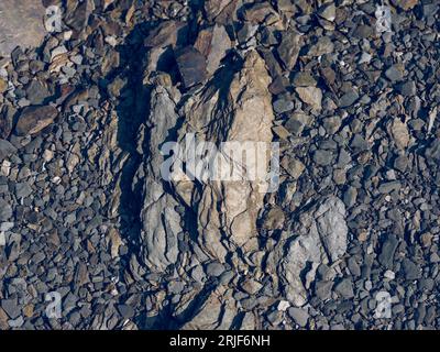 Du dessus du plein cadre de fond texturé de pierres irrégulières rugueuses avec des fissures et des cailloux humides à la lumière du jour Banque D'Images