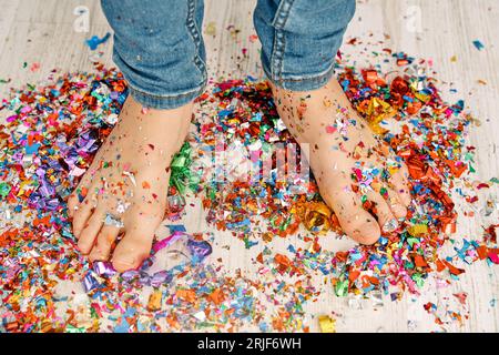 Angle élevé de la récolte anonyme garçon pieds nus en jeans debout sur des confettis colorés dispersés pour la célébration festive Banque D'Images