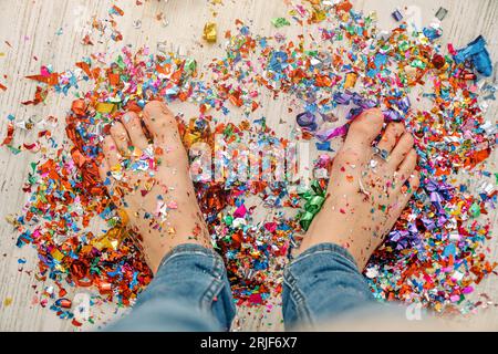 D'en haut de la récolte anonyme garçon pieds nus en jeans debout sur des confettis colorés dispersés sur le sol pour la célébration Banque D'Images