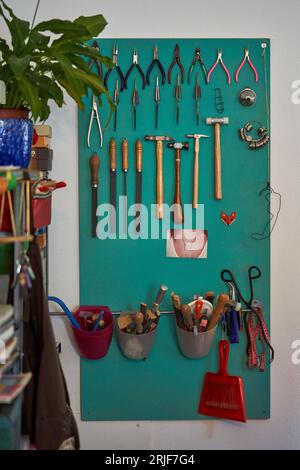 Jeu de pinces coupe-fil limes et marteaux d'établi suspendus en rangée sur le panneau vert sur le mur dans l'atelier traditionnel d'orfèvre Banque D'Images