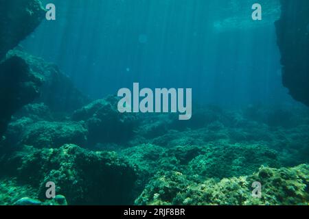 Vue sous-marine des rayons du soleil passant à travers l'eau bleu foncé sur fond rocheux de l'océan Banque D'Images