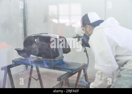 Vue latérale en verre de creux du maître masculin concentré dans le bouchon et le respirateur protecteur peinture réservoir de carburant de moto placé sur le rack avec pulvérisateur pneumatique Banque D'Images