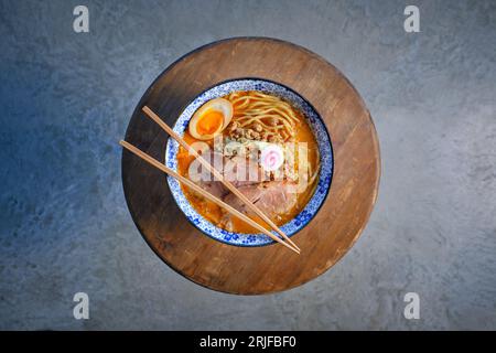 Vue de dessus de la délicieuse soupe de miso ramen avec du porc et des nouilles servies sur une planche de bois avec des baguettes au restaurant Banque D'Images