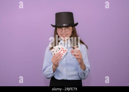 Débutant magicien débutant. Fille avec des cartes dans ses mains dans un chapeau avec un chapeau haut-de-forme et une chemise rayée avec un noeud papillon Banque D'Images