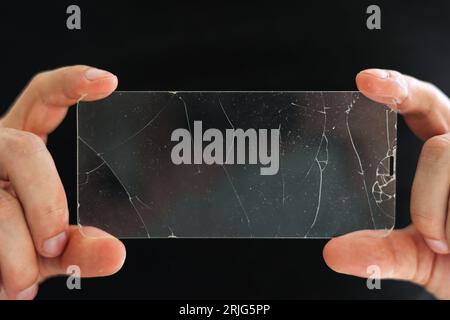 Verre de protection cassé pour l'écran tactile de smartphone dans les mains du réparateur de téléphone sur fond noir. Services pour le collage et le remplacement de pr endommagé Banque D'Images