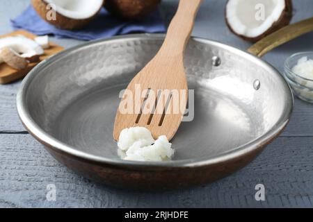 Poêle à frire avec huile de cuisson de noix de coco et spatule sur table en bois gris, gros plan Banque D'Images