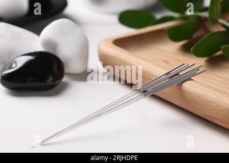 Planche avec des aiguilles d'acupuncture sur une table en bois blanc Banque D'Images