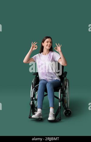 Jeune femme en fauteuil roulant montrant OK sur fond vert Banque D'Images