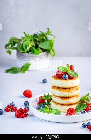 Crêpes épaisses au fromage cottage avec des myrtilles, des framboises et des groseilles rouges, décorées avec de la menthe sur une assiette blanche, délicieux petit déjeuner. Table grise Banque D'Images