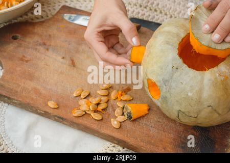 gros plan de mains caucasiennes féminines méconnaissables enlevant la partie pour faire l'œil de citrouille sur une planche à découper en bois, la décorant pour Halloween Banque D'Images