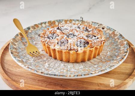 French Flair, clafoutis aux cerises présenté sur marbre blanc avec sucre en poudre et fourchette Banque D'Images