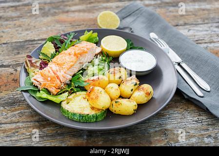 Filet de saumon cuit au four avec des pommes de terre et des légumes sur la table en bois dans l'heure d'été du jardin Banque D'Images