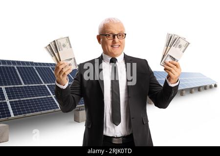 Homme d'affaires mature tenant des piles de billets de banque en dollars américains devant des cellules solaires isolées sur fond blanc Banque D'Images