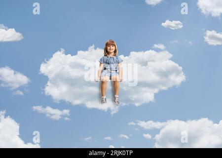 Petite fille assise sur un nuage et souriant dans le ciel Banque D'Images