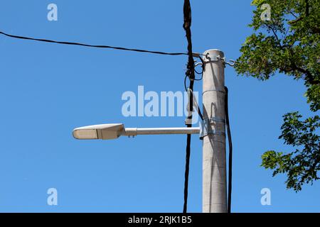 Ancien lampadaire de rue boîtier en plastique gris clair amélioré avec des lumières LED modernes maintenues par quatre vis sur le dessus d'un poteau métallique unique monté sur béton solide Banque D'Images