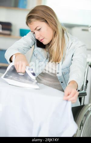 jeune femme au téléphone repassant des vêtements Banque D'Images