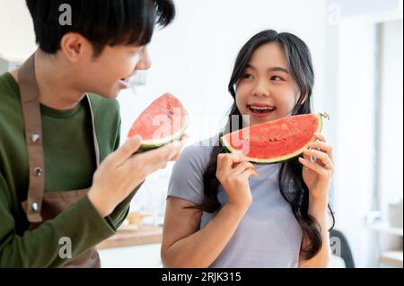 Un jeune couple asiatique charmant et joyeux aime manger de la pastèque ensemble dans la cuisine, passer du temps amusant ensemble à la maison. Date de cuisson, do romantique Banque D'Images