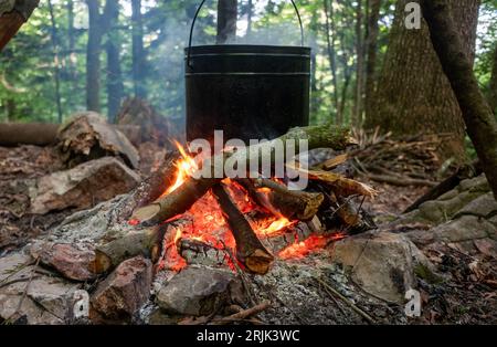 L'eau bout dans un pot noir sur le feu d'un feu de camp dans une clairière forestière dans les montagnes. Banque D'Images