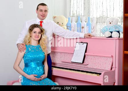 Attrayant jeune couple célèbre les vacances à la maison. Debout sur le fond d'un beau piano rose. Le mari embrasse sa femme enceinte. Un homme Banque D'Images