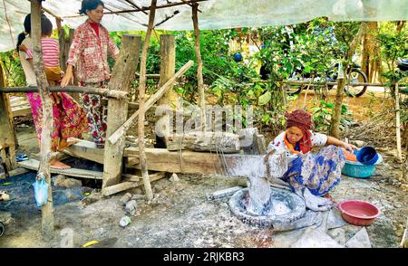 Battambang, Cambodge - 29 février 2012. Les femmes utilisent un grand mortier en bois et un pilon pour broyer du riz imbibé et cru en une pâte qui sera du papier de riz Banque D'Images