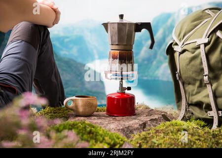 Cuisiner, faire du café ou du thé sur un brûleur à gaz de camping portable avec une bouteille de gaz rouge avec un fond de nature scandinave. Randonnée estivale, écotourisme, survie. Banque D'Images