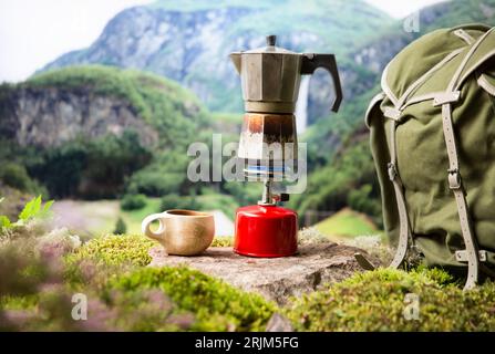 Cuisiner, faire du café ou du thé sur un brûleur à gaz de camping portable avec une bouteille de gaz rouge avec un fond de nature scandinave. Randonnée estivale, écotourisme, survie. Banque D'Images