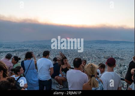 Le 22/08/2023 un feu de forêt a commencé sur les contreforts de la montagne Parnitha dans la banlieue ouest d'Athènes, Grèce. Alimentée par des vents violents, elle a rapidement grandi et brûlé des maisons et des commerces. Cette photo est de la colline de Lycabette, où les touristes et les habitants regardent le feu. Banque D'Images