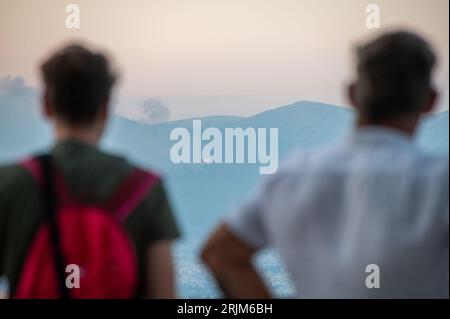 Le 22/08/2023 un feu de forêt a commencé sur les contreforts de la montagne Parnitha dans la banlieue ouest d'Athènes, Grèce. Alimentée par des vents violents, elle a rapidement grandi et brûlé des maisons et des commerces. Cette photo est de la colline de Lycabette, où les touristes et les habitants regardent le feu. Banque D'Images