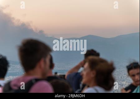 Le 22/08/2023 un feu de forêt a commencé sur les contreforts de la montagne Parnitha dans la banlieue ouest d'Athènes, Grèce. Alimentée par des vents violents, elle a rapidement grandi et brûlé des maisons et des commerces. Cette photo est de la colline de Lycabette, où les touristes et les habitants regardent le feu. Banque D'Images