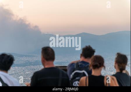 Le 22/08/2023 un feu de forêt a commencé sur les contreforts de la montagne Parnitha dans la banlieue ouest d'Athènes, Grèce. Alimentée par des vents violents, elle a rapidement grandi et brûlé des maisons et des commerces. Cette photo est de la colline de Lycabette, où les touristes et les habitants regardent le feu. Banque D'Images