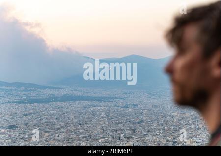 Le 22/08/2023 un feu de forêt a commencé sur les contreforts de la montagne Parnitha dans la banlieue ouest d'Athènes, Grèce. Alimentée par des vents violents, elle a rapidement grandi et brûlé des maisons et des commerces. Cette photo est de la colline de Lycabette, où les touristes et les habitants regardent le feu. Banque D'Images