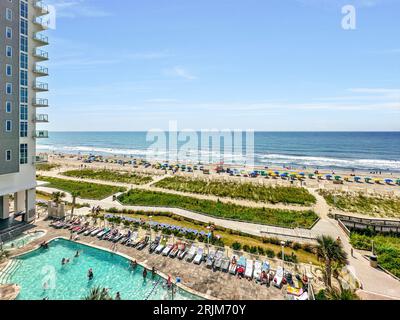 Une vue aérienne d'un complexe avec un océan bleu étincelant, une plage de sable blanc et une piscine avec chaises longues et parasols Banque D'Images