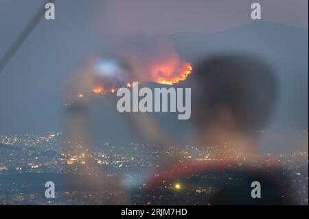 Le 22/08/2023 un feu de forêt a commencé sur les contreforts de la montagne Parnitha dans la banlieue ouest d'Athènes, Grèce. Alimentée par des vents violents, elle a rapidement grandi et brûlé des maisons et des commerces. Cette photo est de la colline de Lycabette, où les touristes et les habitants regardent le feu. Banque D'Images