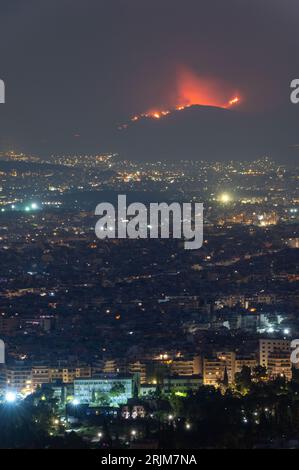 Le 22/08/2023 un feu de forêt a commencé sur les contreforts de la montagne Parnitha dans la banlieue ouest d'Athènes, Grèce. Alimentée par des vents violents, elle a rapidement grandi et brûlé des maisons et des commerces. Cette photo est de la colline de Lycabette la nuit quand le feu brûlait encore. Banque D'Images