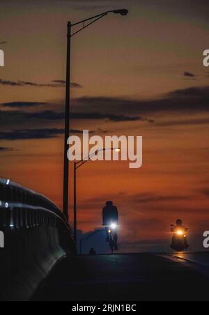 Une personne adulte qui roule à vélo sur une autoroute faiblement éclairée le soir, éclairée par les phares lumineux Banque D'Images