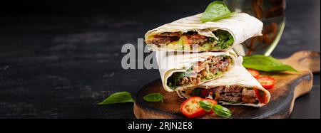 Wraps tortilla grillés avec du bœuf et des légumes frais sur une planche de bois. Burrito de boeuf. Cuisine mexicaine. Concept de nourriture saine. Bannière Banque D'Images