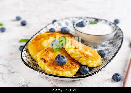 Crêpes au fromage cottage avec de la crème sure et des myrtilles sur un fond clair. Petit déjeuner ou déjeuner. Banque D'Images