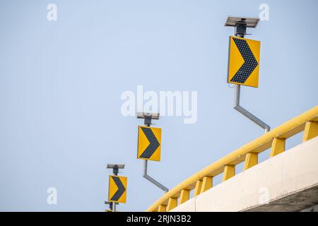 Des panneaux de signalisation jaunes guident les conducteurs le long des virages. Les symboles assurent la sécurité lorsqu'ils naviguent dans les rues sous le ciel bleu vigilant. Signe fléché Banque D'Images