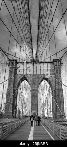 Une photo verticale en niveaux de gris de personnes marchant sur le pont de Brooklyn à New York, aux États-Unis Banque D'Images