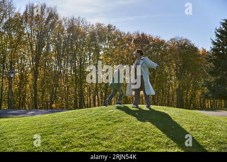 mère et fils joyeux, femme afro-américaine debout sur une colline verte avec un garçon, journée ensoleillée, automne Banque D'Images