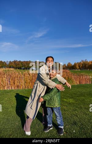 liaison, nature automnale, mère afro-américaine heureuse embrassant son fils, famille dans les vêtements d'extérieur, automne Banque D'Images