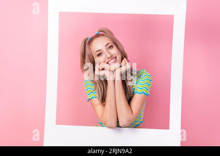 Portrait de jolie fille joyeuse avec des queues habillées de costume coloré mains sur le menton posant dans le cadre photo isolé sur fond de couleur rose Banque D'Images