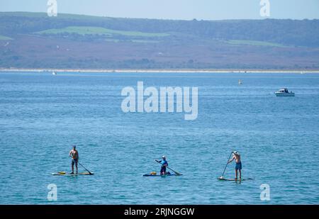 Les gens paddle board dans la mer au large de la plage de Bournemouth dans le Dorset. Une vague de chaleur mise en place pour balayer le pays mercredi pourrait être la dernière cette année, ont dit les prévisionnistes. Le met Office s'attend à ce que les températures atteignent un pic à la fin des années 20 dans certaines zones avant que les chutes de mercure et le soleil ne laissent place à des conditions plus instables pendant le jour férié.Date de la photo : mercredi 23 août 2023. Banque D'Images