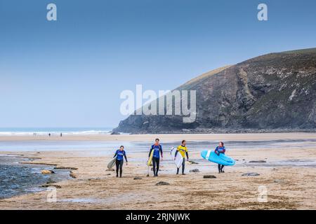 Trois surfeurs novices et leur instructeur de surf portant leurs planches de surf après une leçon de surf à Mawgan Porth à Cornwall au Royaume-Uni. Banque D'Images