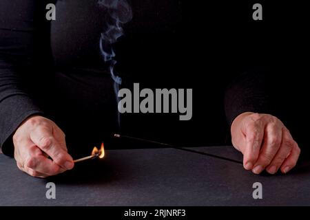 Mains de femme allumant un bâton d'encens avec une allumette avec un fond noir et un espace de copie Banque D'Images