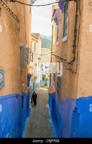 Homme marchant dans une rue étroite avec des murs peints en bleu et des escaliers dans la médina de la ville de Chefchaouen, Maroc. Banque D'Images